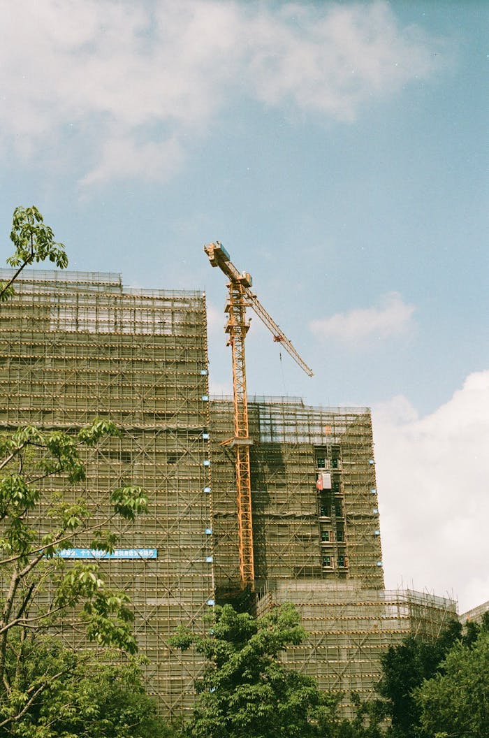 High angle shot of an urban construction site featuring a crane and scaffolding against a blue sky.